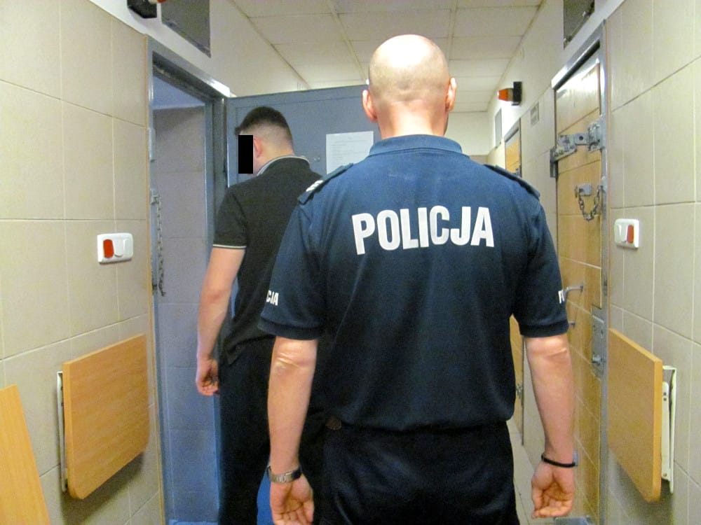 Policjant eskortujący podejrzanego korytarzem więziennym. POLICJA