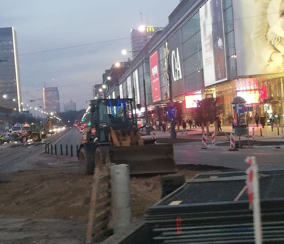 Budowa ulicy w Warszawie o zmierzchu, spychacz pracuje w pobliżu sklepów.