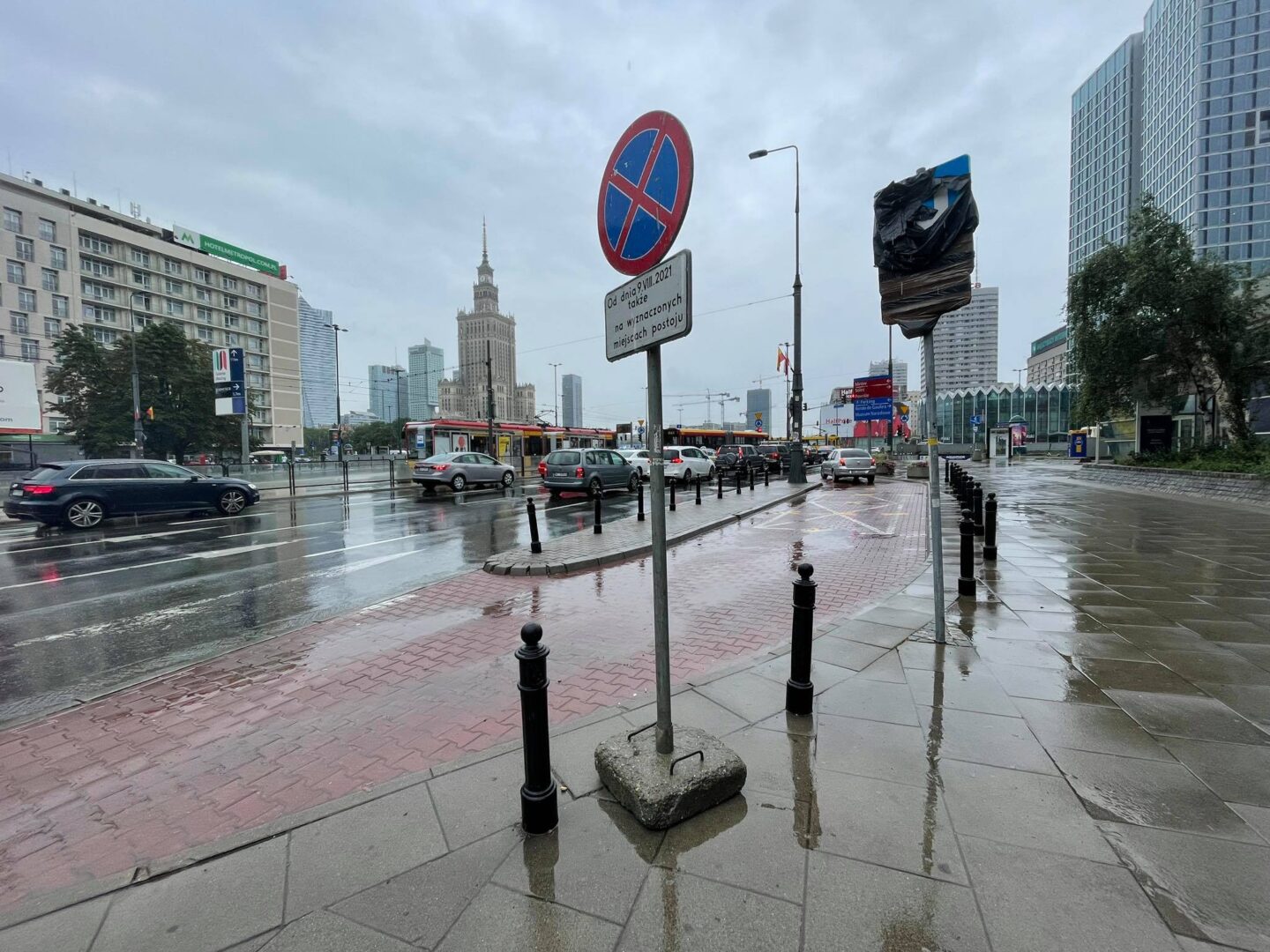 Deszczowa ulica Warszawy. W tle widać znak zakazu parkowania i Pałac Kultury i Nauki.