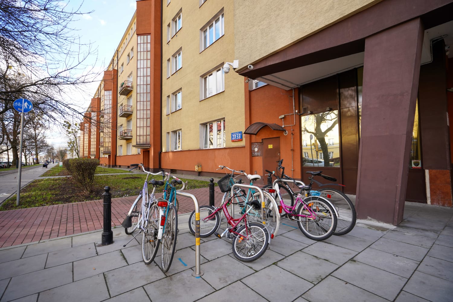 Rowery przypięte do stojaka na zewnątrz budynku mieszkalnego.