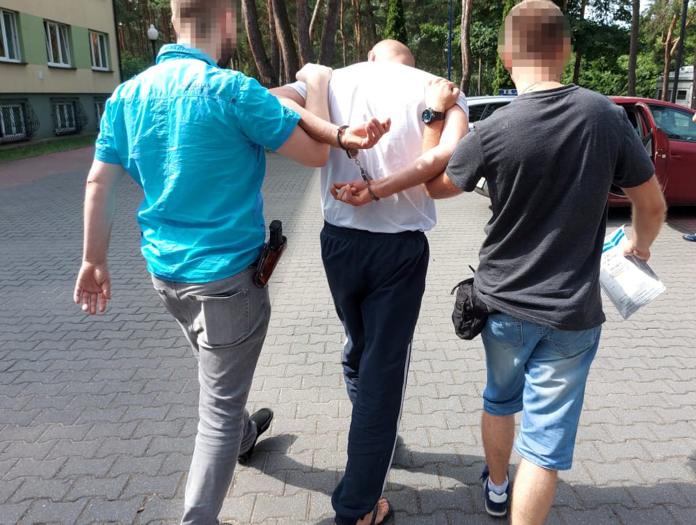 Dwóch policjantów eskortuje skutego mężczyznę.