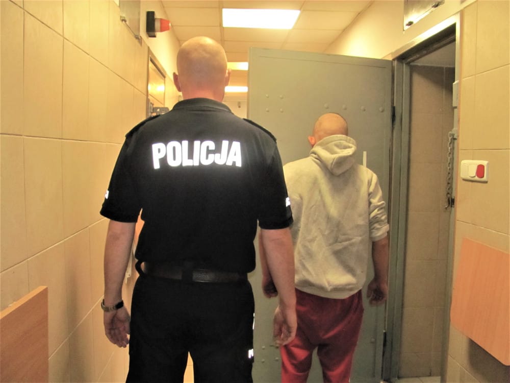 Policjant eskortujący podejrzanego korytarzem więziennym. POLICJA