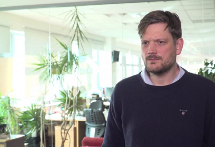 Mężczyzna w ciemnym swetrze przemawia w nowoczesnym biurze