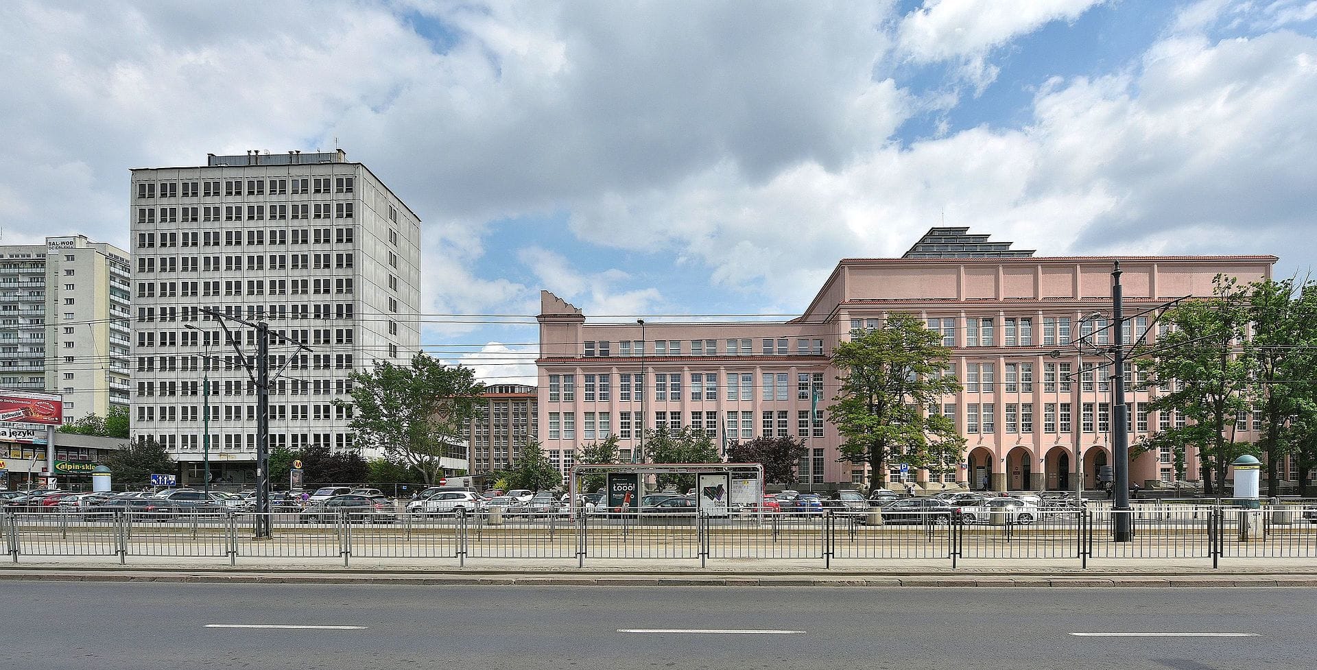 Scena uliczna Warszawy z nowoczesnymi i zabytkowymi budynkami, w tym różowym budynkiem i wysokim szarym budynkiem.