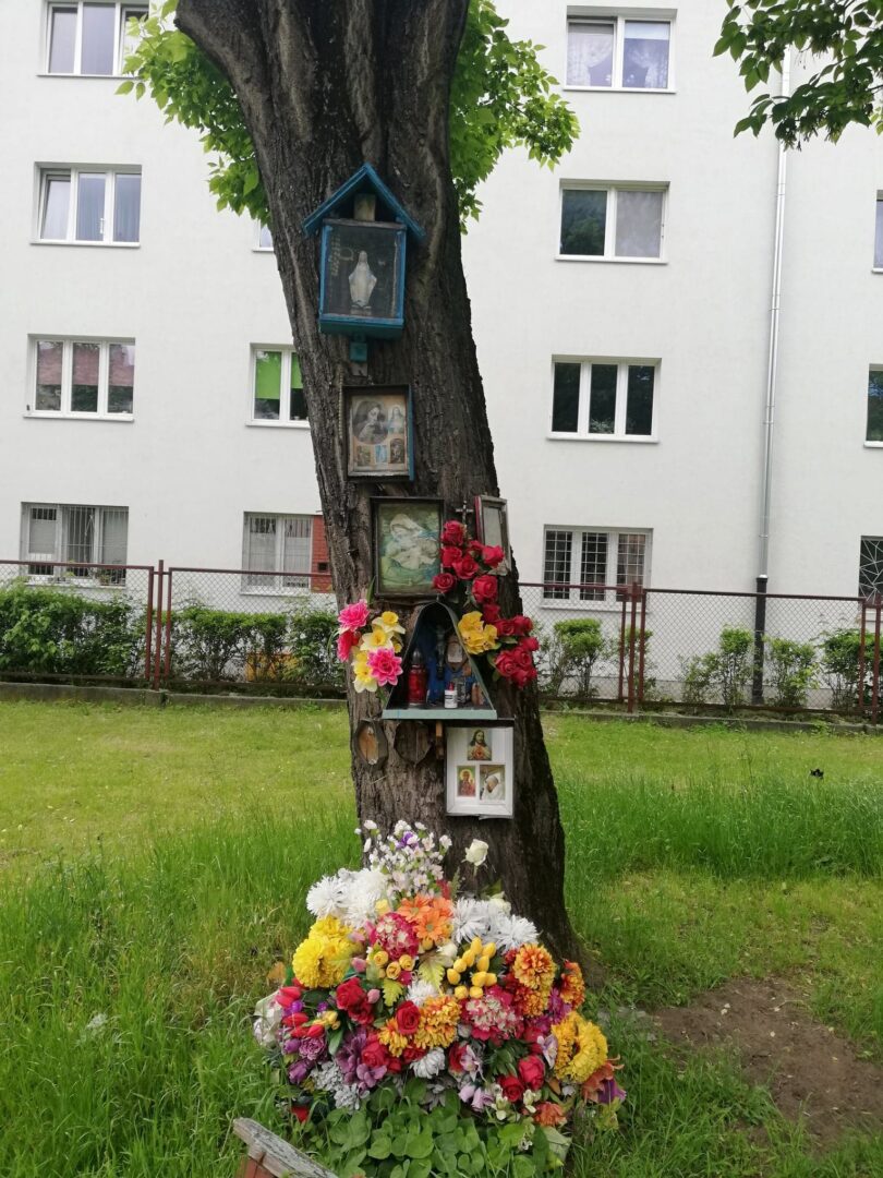 Świątynia religijna na drzewie ozdobiona kwiatami i ikonami religijnymi.