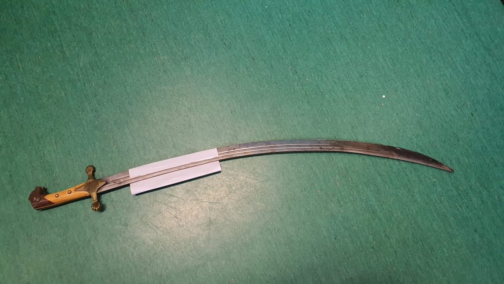 Antyczny miecz mameluków z ozdobną rękojeścią, prezentowany na zielonej powierzchni.