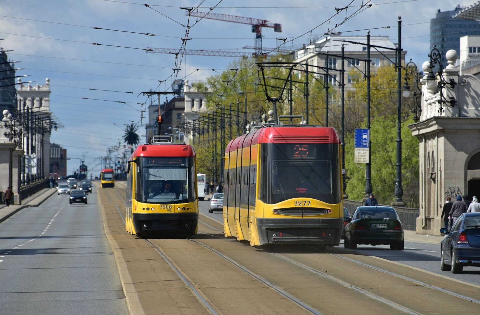 Dwa nowoczesne tramwaje o numerach 3208 i 3277 jadą ulicą miasta.