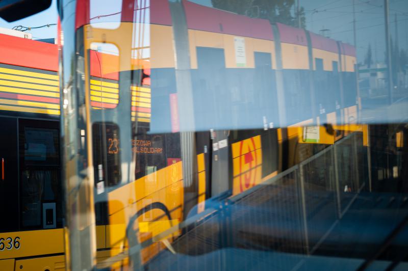 Odbicie żółto-czerwonego tramwaju nr 23, pokazujące przystanek "Szczawa Solidarni".