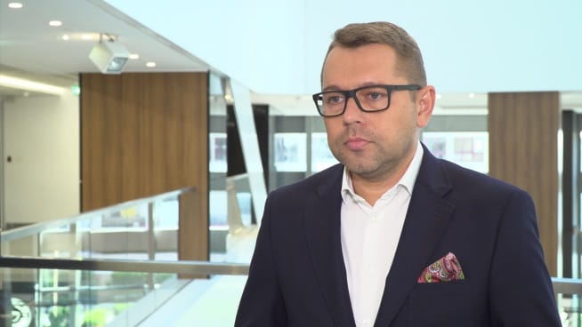 Mężczyzna w garniturze i okularach przemawia podczas rozmowy kwalifikacyjnej.