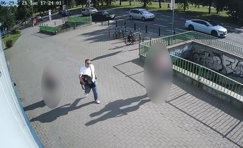 Mężczyzna niosący torbę przechodzi obok przejścia podziemnego, obok zaparkowanych samochodów i rowerów.