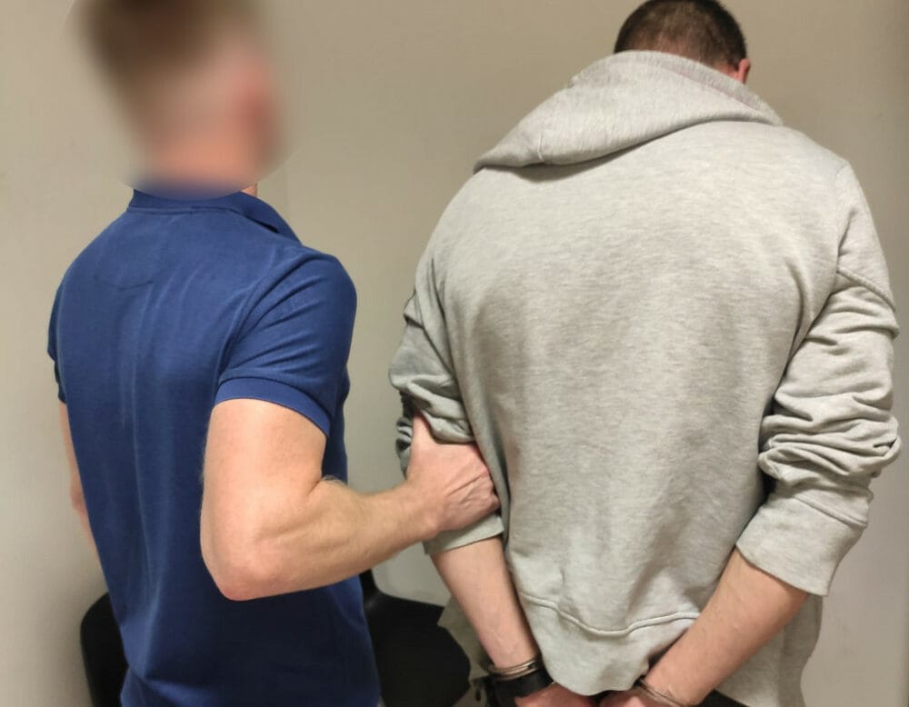 Policjant aresztujący podejrzanego z rękami skutymi z tyłu.