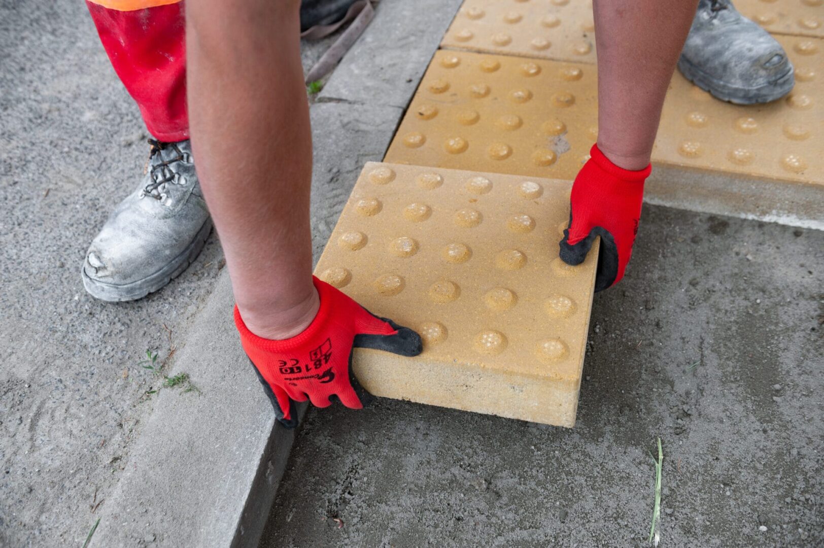 Pracownik układający nawierzchnię dotykową, układający teksturowaną kostkę brukową.