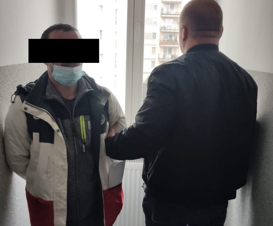 Policjant aresztujący podejrzanego w masce na twarzy.