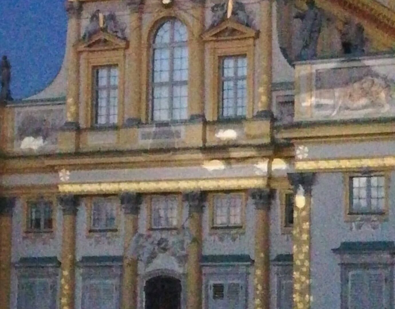 Bogato zdobiona barokowa fasada pałacu ze złotymi detalami i wieloma oknami.