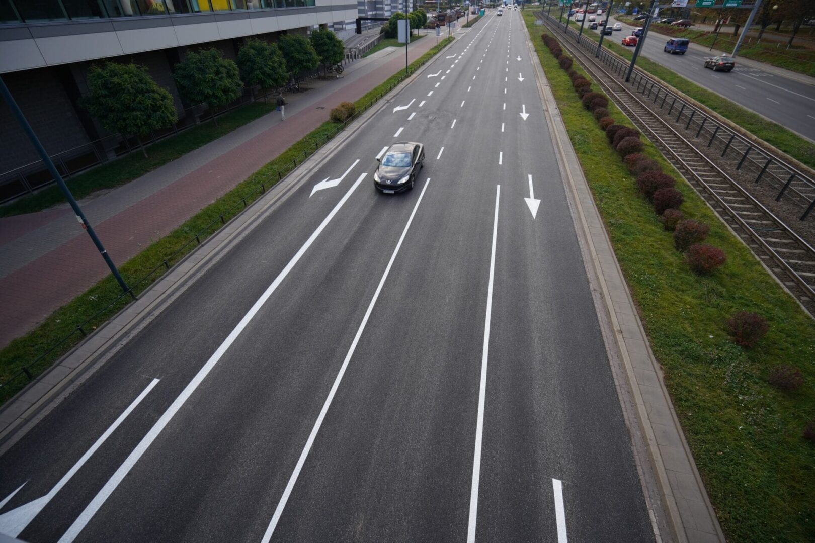 Widok z góry na ulicę miejską z samochodem jadącym po pasie oznaczonym białymi liniami i strzałkami.