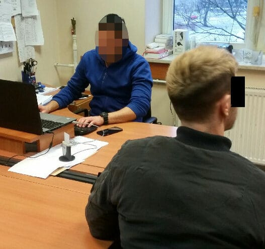 Dwóch mężczyzn siedzi przy stole, jeden używa laptopa. Przesłuchanie przez policję?