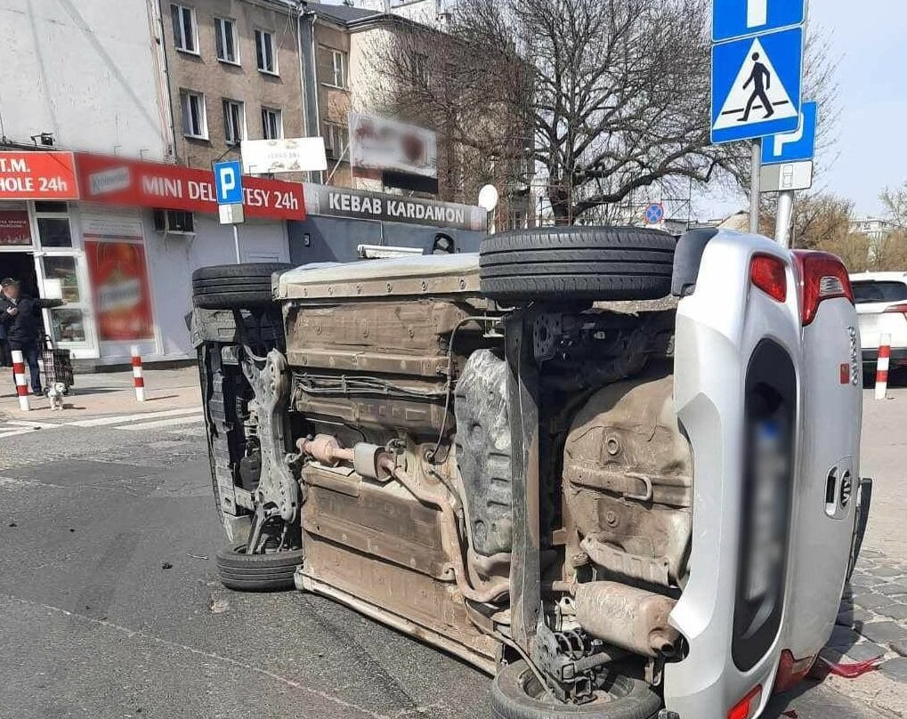 Srebrny samochód przewrócony na ulicy miejskiej po wypadku