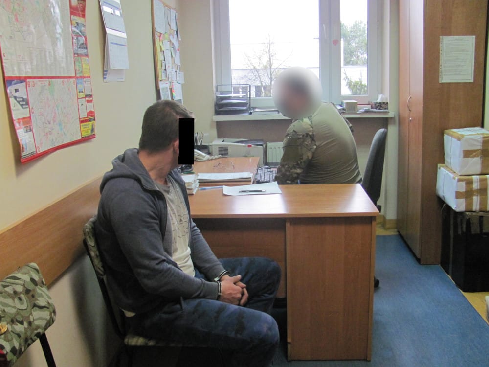 Dwóch mężczyzn w kajdankach siedzi przy biurku w biurze podczas przesłuchania.