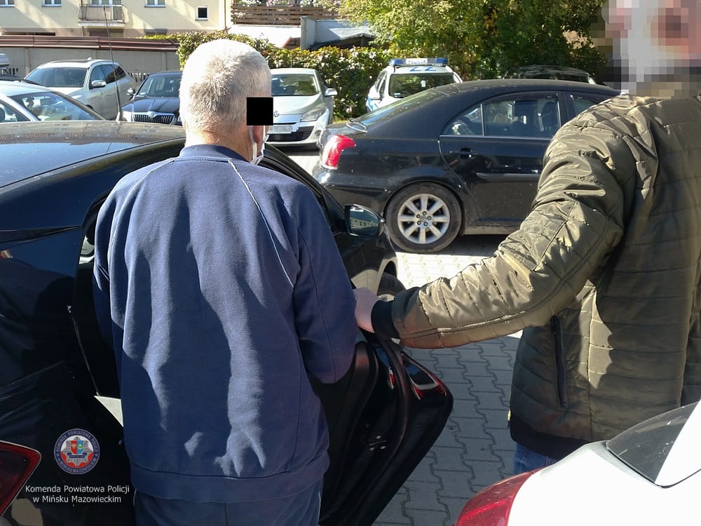 Policjant pomaga mężczyźnie wsiąść do samochodu podczas aresztowania.