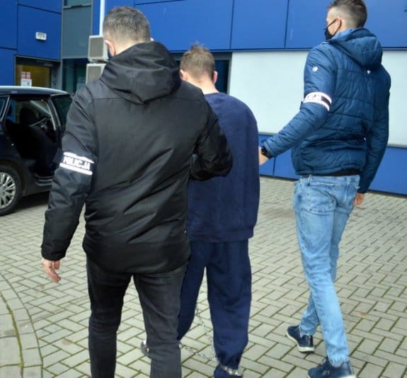 Policjanci eskortujący podejrzanego w kajdankach