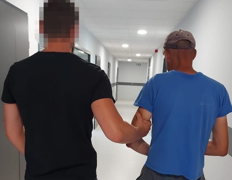 Dwóch mężczyzn idzie korytarzem szpitalnym, jeden pomaga drugiemu.