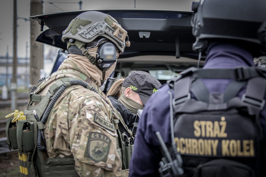 Policjanci w mundurach taktycznych podczas operacji. Na kamizelce jednego z funkcjonariuszy widoczny jest napis „Straż Ochrony Kolei”.