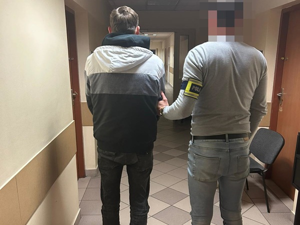 Policjant eskortujący podejrzanego korytarzem.