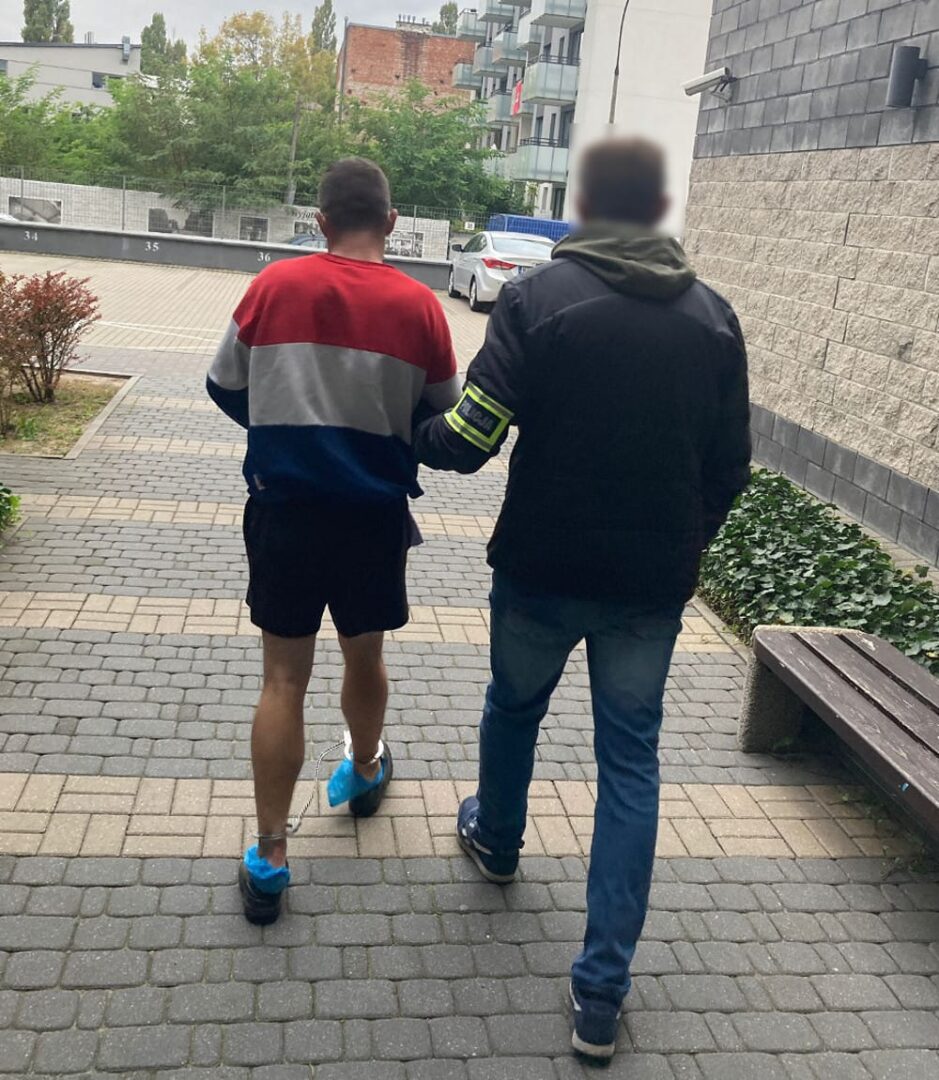 Policjant eskortujący podejrzanego w kajdankach