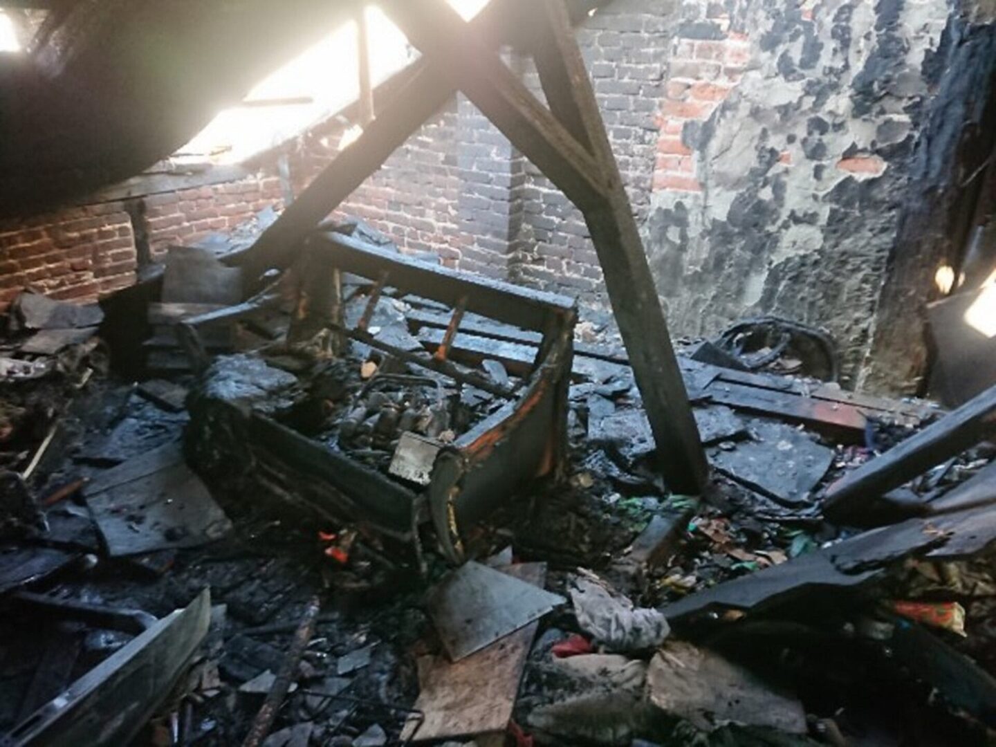 Skutki pożaru domu, pokazujące poważne zniszczenia poddasza i mebli.